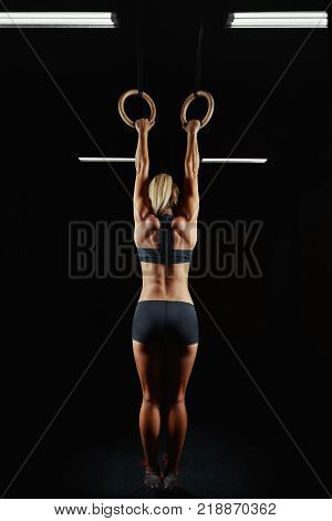 Full length rearview shot of a female athlete performing pull-ups on gymnastic rings. Fitness woman with strong beautiful body exercising on gym rings health power endurance competitive