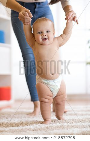 Cute baby taking first steps holding mother hands