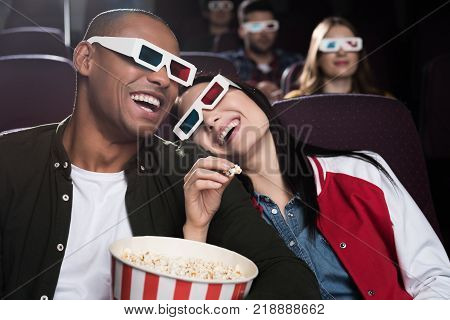 happy interracial couple in 3d glasses eaying popcorn and watching movie in cinema