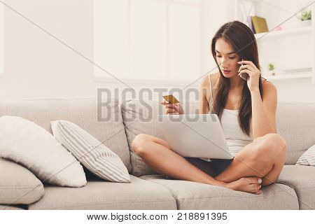 Seious girl shopping online on laptop. Smiling young woman with credit card making order on mobile from cozy home. Easy buying and technology concept
