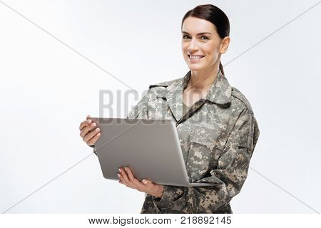 Computer technology. attractive woman in combat uniform looking straight while standing on the isolated background and carrying laptop