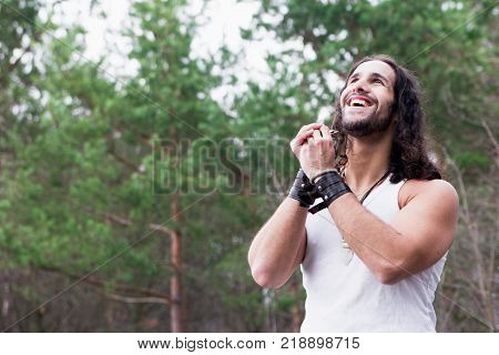 Young man playing the harmonica in a forest glade. Man laughs happily. Young Man standing alone outdoor Travel Lifestyle concept