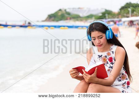 Asian girls read the books and listen to classical music with the blue headphones at the beach, lonely with white summer dresses relaxing in the tropical sea.
