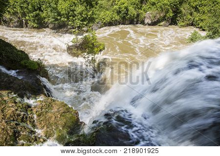 Croatian Village Of Rastoke By A River Canyon With Wooden Houses In A Green Lanscape With Trees And