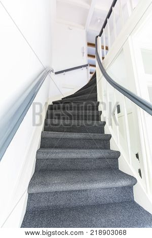 stiff staircase with grey carpet and white walls viewed from bottom up