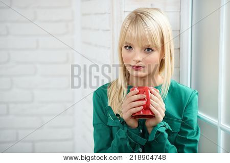 Close up portrait of a young attractive charming blonde haired woman looking to the camera holding a cup of hot coffee copyspace leisure lifestyle recreation weekend holidays drinking.