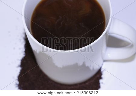 Coffee in a white mug with ground coffee beans surrounding it