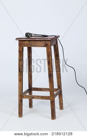 This is a photo of a microphone sitting on top of a wooden stool lite from above. Shot on a white background.