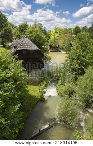 Croatian Village Of Rastoke By A River Canyon With Wooden Houses In A Green Landscape With Trees And