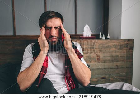 picture from a young man with handkerchief. Sick guy lies in bed and has runny nose. man makes a cure for the common cold Model male has a high temperature, headache, migraine.