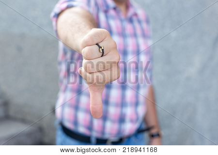 Upset man showing thumb-down sign to dislike. Displeased man giving estimation meaning negative reaction outdoors. Body language concept
