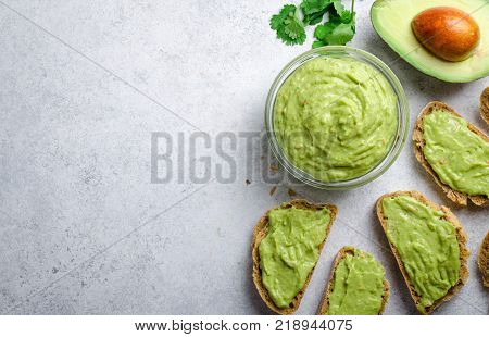 Traditional mexican homemade guacamole sauce in a glass bowl and sliced bread on a light gray stone background. Top view, copy space, horizontal image