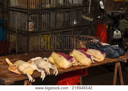 Poultry chicken plucked of feathers bare naked raw fresh on chopping board of wet dry market food vendor stalls along street of East Asia city. China