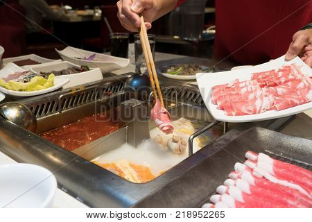 a red shirt women is cooking the Chinese shabu hotpot