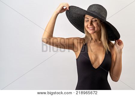 large contrast Studio portrait of an attractive Caucasian woman with long blond hair in black bikini and hat posing with a big smile with teeth