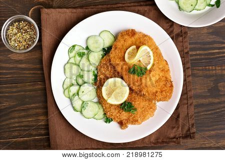Schnitzel with cucumber salad on plate over wooden table. Top view flat lay