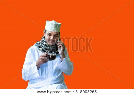 Muslim Business Man In White Hajab Dress Hand Hold Cup Of Black Coffee And Use Smart Mobile Phone Ta