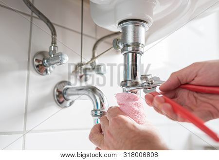 Man Repairing Sink Trap With Adjustable Pipe Wrench In Bathroom