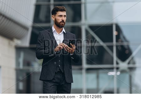 Businessman Using Smartphone And Smiling At Airport. Young Business Executive With Mobile Phone At A