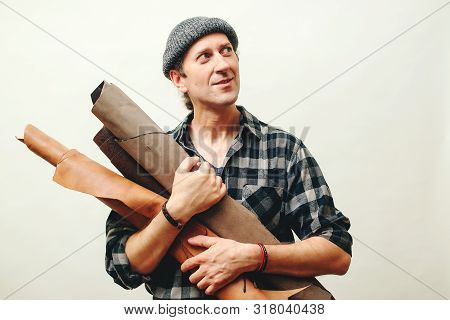 Artisan In Plaid Shirt, Holds Set Of Leather In His Workshop. Master Has Idea For New Leather Produc