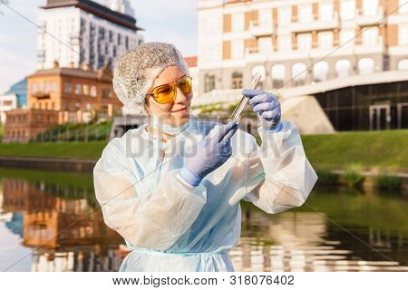 Female Ecologist Or Epidemiologist Visually Assesses The Quality Of Water In An Urban River, Looking