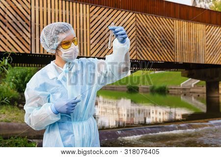Female Ecologist Or Epidemiologist Visually Assesses The Quality Of Water In An Urban River, Looking
