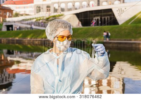 Female Ecologist Or Epidemiologist Visually Assesses The Quality Of Water In An Urban River, Looking
