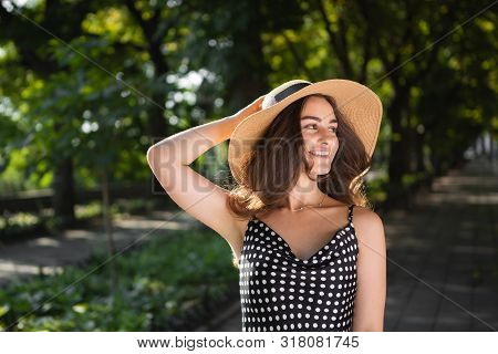 Close-up Porttrait Of A Beautiful Young Brunette Woman Dressed In A Black Dress And A Hat With Wide 