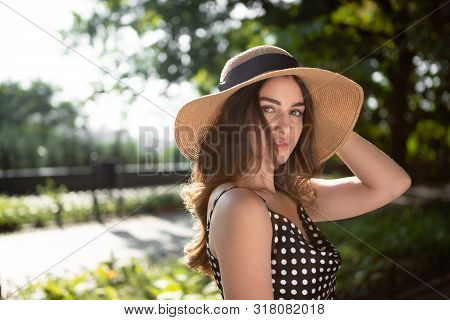 Close-up Porttrait Of A Beautiful Young Brunette Woman Dressed In A Black Dress And A Hat With Wide 
