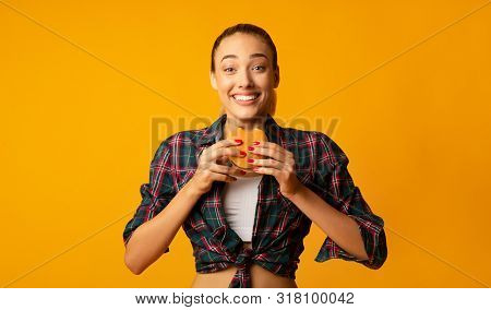 Cheat Meal Concept. Millennial Girl Eating Burger Over Yellow Background In Studio. Empty Space For 