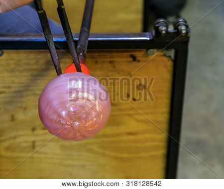 Glass Blower Shaping A Bubble Of Melted Glass On A Rod By Hand In The Manufacturing Process At A Gla