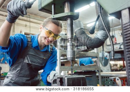 Woman worker in metal workshop using pedestal drill to work on piece