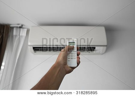 Mans Hand Using Remote Controler. Hand Holding Rc And Adjusting Temperature Of Air Conditioner Mount