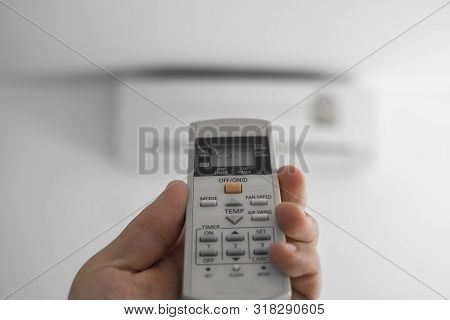 Mans Hand Using Remote Controler. Hand Holding Rc And Adjusting Temperature Of Air Conditioner Mount