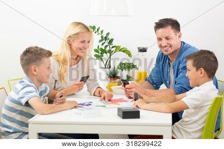 Happy Young Family Playing Card Game At Dining Table At Bright Modern Home.