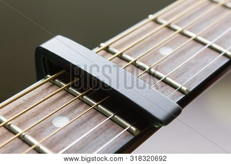 Black Capo On Acoustic Guitar String And Fingerboard With Soft Natural Light In Close Up View