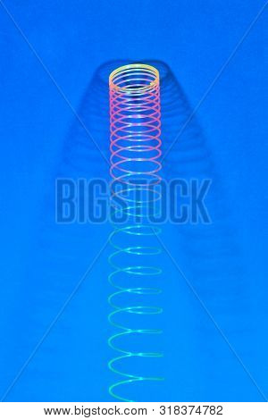 Stratching colorful plastic spiral toy with two shadows on a blue background, place for text.