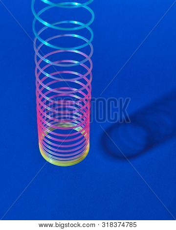 Stretching rainbow plastic slinky toy above blue background with shadows, place for text.