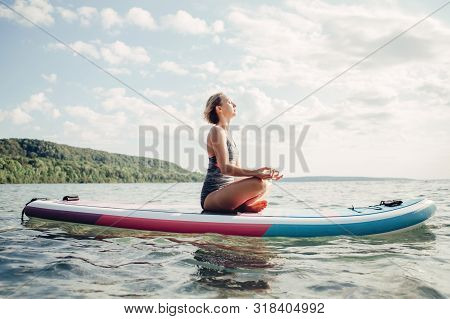 Middle Age Caucasian Woman Practising Yoga On Paddle Sup Surfboard At Sunset. Female Stretching Doin