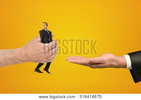 Big Male Hand Passing Tiny Businessman To Another Hand On Yellow Background
