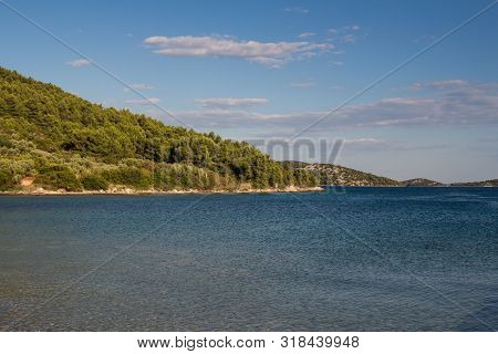 Empty Beach With Rocky Coast. Blue Clean Water Of The Adriatic Sea With Small Waves. Hill With A For