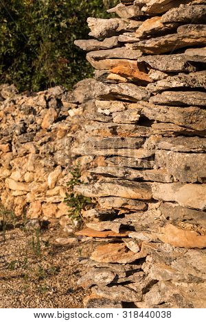 Stone Wall Made Of Various Natural Tones Of A Brown Color, Located Outdoors, Enlighted By Sunlight. 