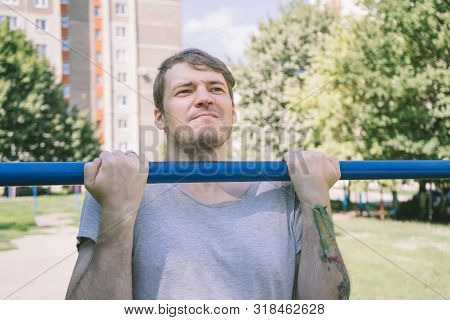 A Young Handsome Man In Casual Clothes Is Doing Pull Up Exercise On Horizontal Bar. Fitness, Sport, 