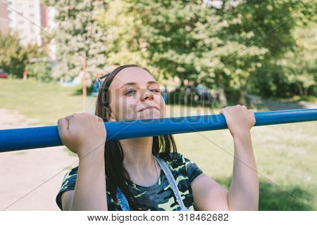 A Young Handsome Woman In Casual Clothes Is Doing Pull Up Exercise On Horizontal Bar. Fitness, Sport
