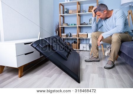Man Sitting On Sofa In Front Fallen Television With Broken Screen