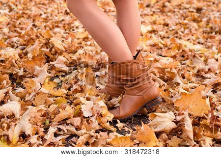Female Legs In Brown Boots. Yellow Foliage Underfoot. Autumn Concept