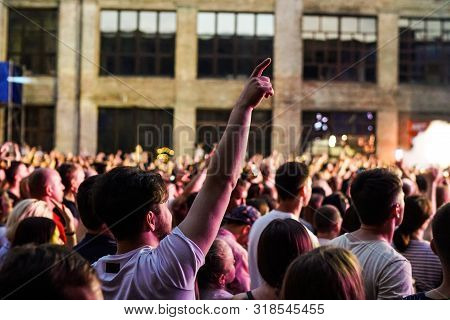 Concert Crowd Attending A Concert, People Silhouettes Are Visible, Backlit By Stage Lights. Raised H