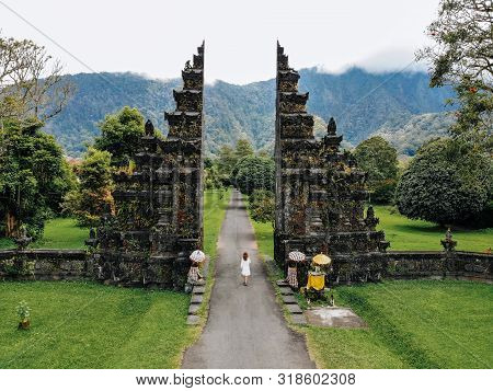 Tourist Woman In White Dress Walking Through Traditional Balinese Hindu Gate Candi Bentar Close To B