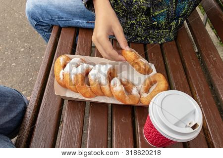 A Teen Boy Sitting On A Bench In Park And Eating Beignet Pastries, Donuts And Drinking Coffee Or Tea