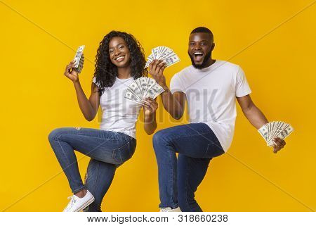 African American Cheerful Couple Dancing With Money In Their Hands, Lifting Legs Up